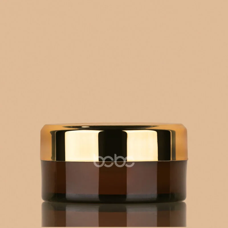 Small amber glass jar with a reflective gold-colored screw-on lid, suitable for cosmetic creams or balms.